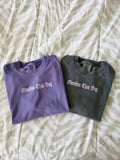 Manifest That Bag unisex motivational tee in pepper and grape – flat lay